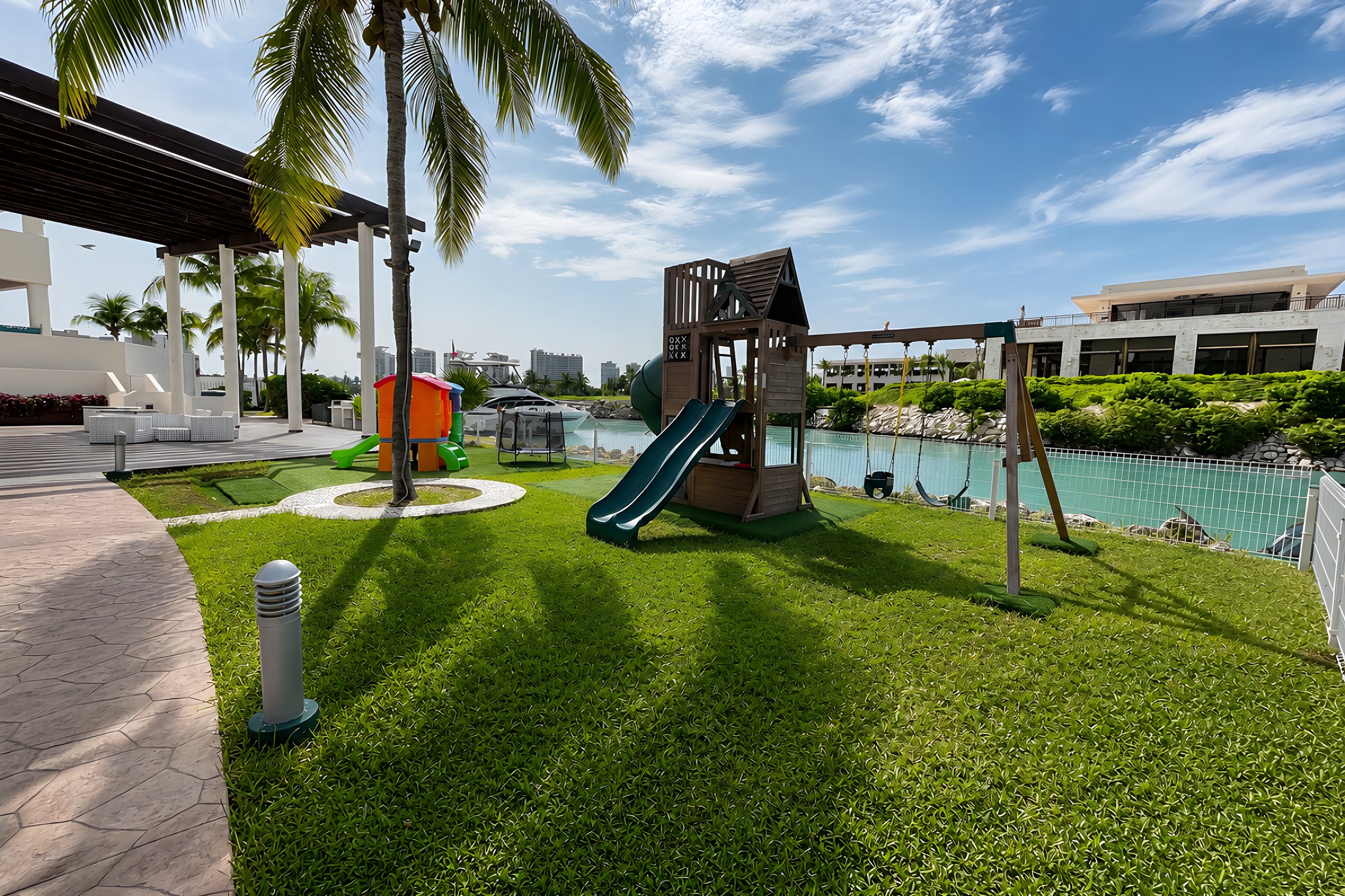 Área infantil con juegos y resbaladilla entre jardines en Maioris Marina Residences, Puerto Cancún