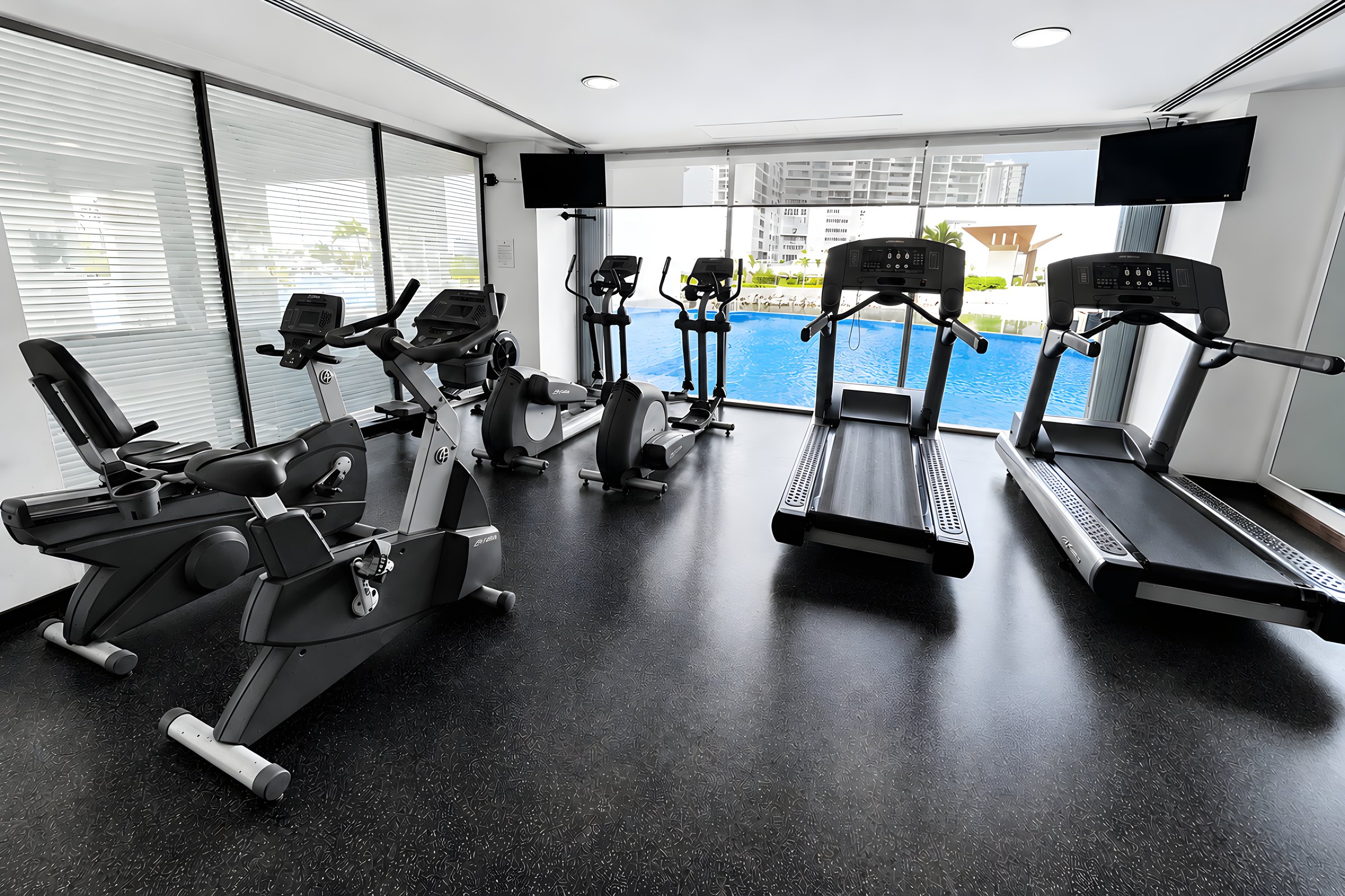 Bicicletas y caminadoras frente a la alberca en el gimnasio de Maioris Marina Residences, Puerto Cancún