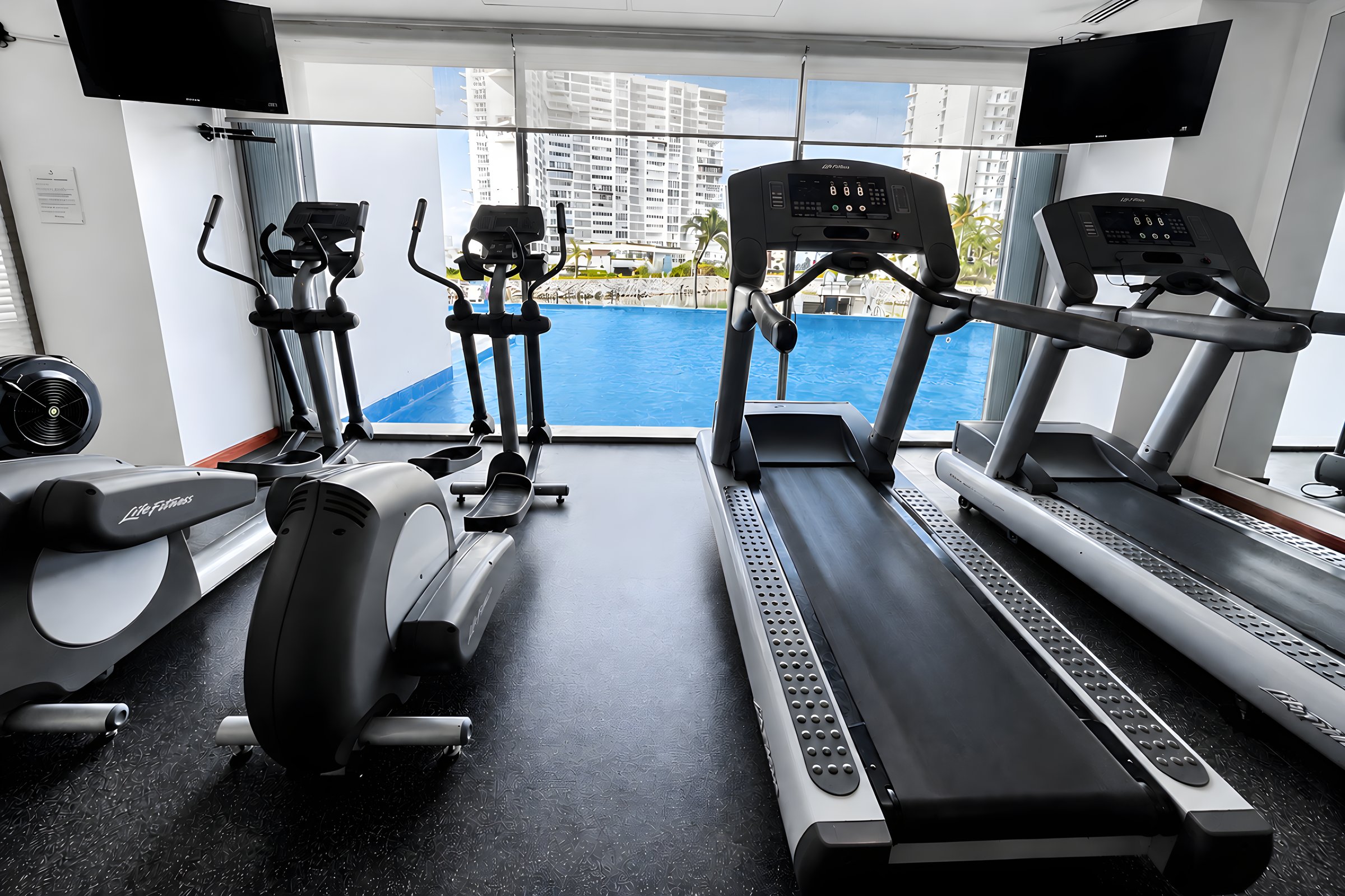 Gimnasio con equipo de cardio frente a un ventanal con vista a la alberca en Maioris Marina Residences, Puerto Cancún