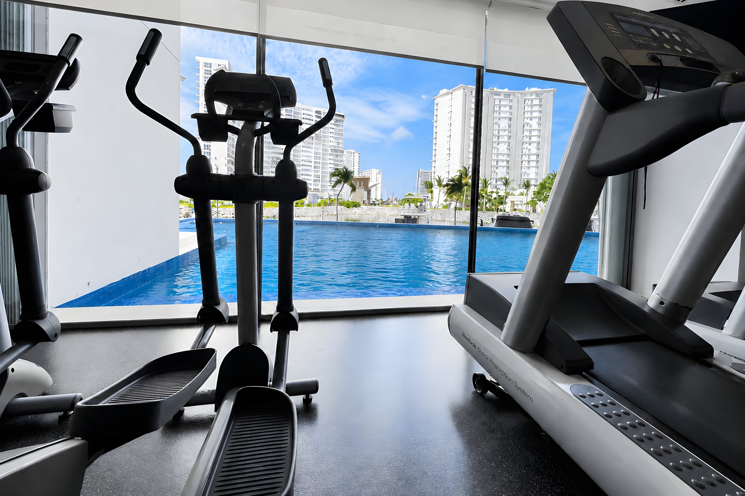Gimnasio con equipo de cardio frente a un ventanal con vista al canal en Maioris Marina Residences, Puerto Cancún