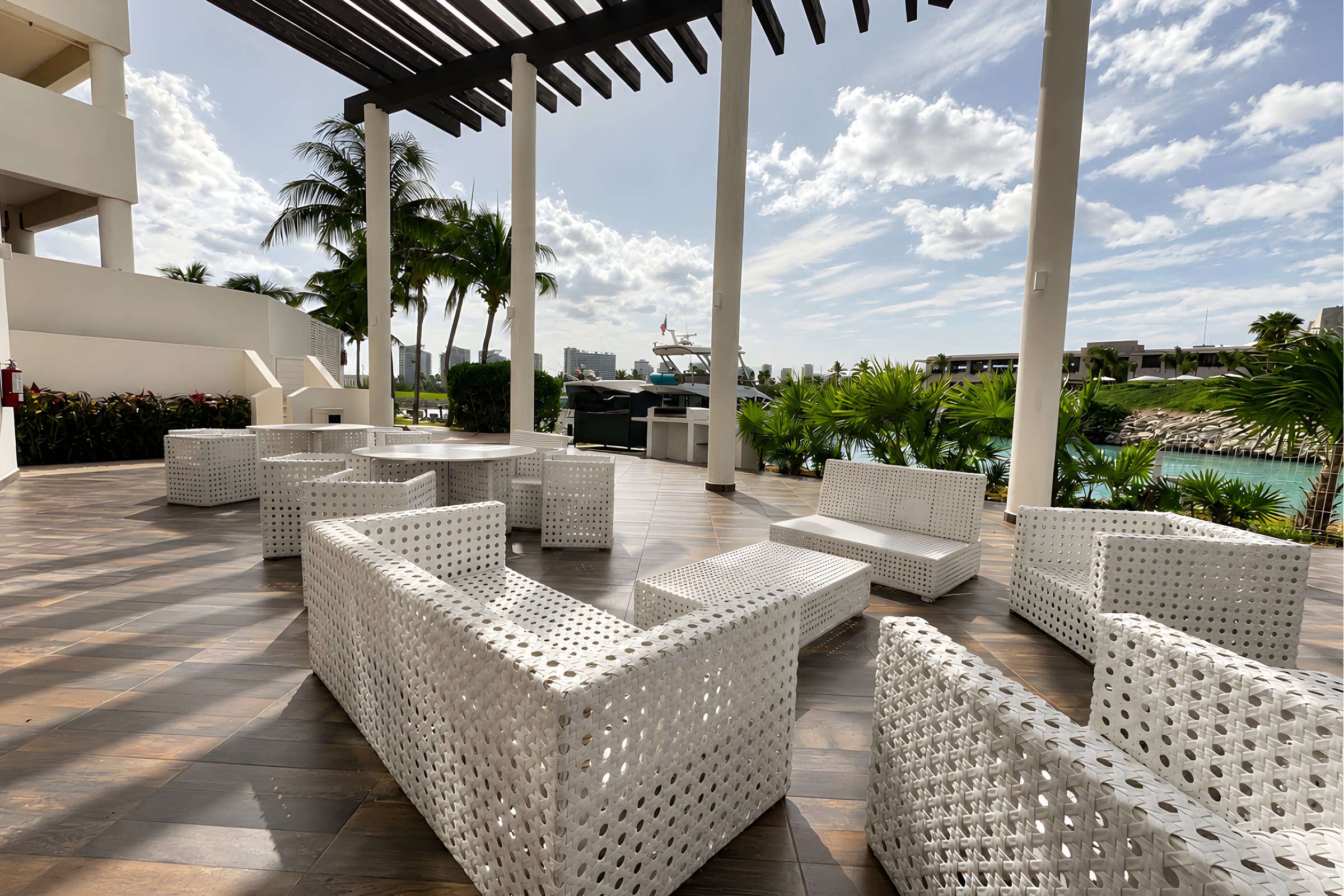 Lounge exterior con sofás blancos y jardines en Maioris Marina Residences, Puerto Cancún