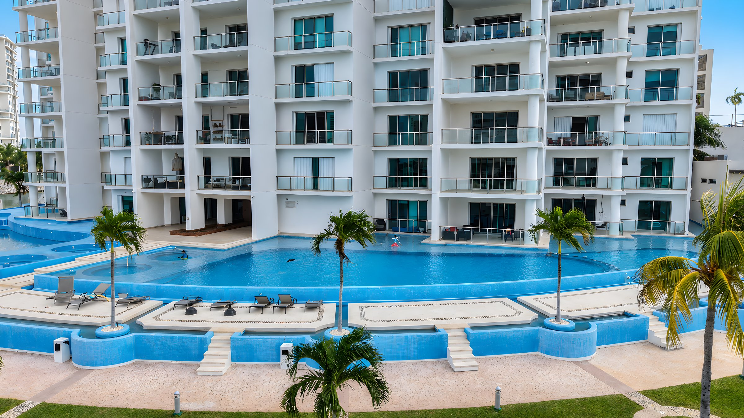 Alberca jardín con palmeras al pie de la torre de Maioris Marina Residences, Puerto Cancún
